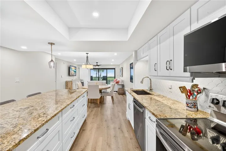 Kitchen with stainless steel appliances, white cabinets, light wood-style floors, pendant lighting, and open floor plan