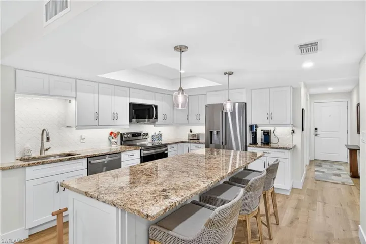 Kitchen with decorative backsplash, white cabinets, light wood-style floors, stainless steel appliances, and recessed lighting
