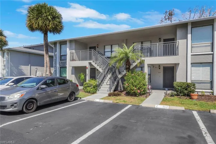 View of property with stairway and uncovered parking