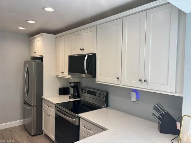 Kitchen with stainless steel appliances, white cabinetry, light stone countertops, recessed lighting, and wood finished floors