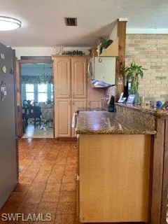 Kitchen with light brown cabinetry, dark stone countertops, and stainless steel refrigerator