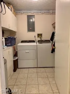 Clothes washing area with electric panel, washing machine and clothes dryer, cabinets, and light tile patterned floors