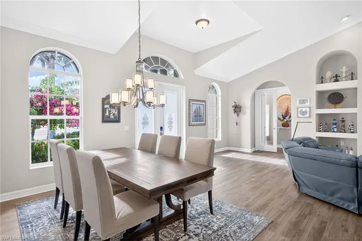Dining space featuring arched walkways, light wood finished floors, built in shelves, a chandelier, and french doors