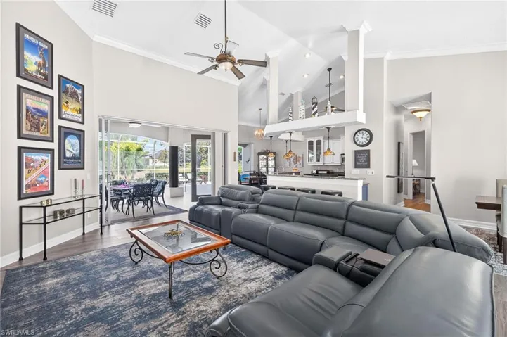 Living room with wood finished floors, high vaulted ceiling, crown molding, and ceiling fan