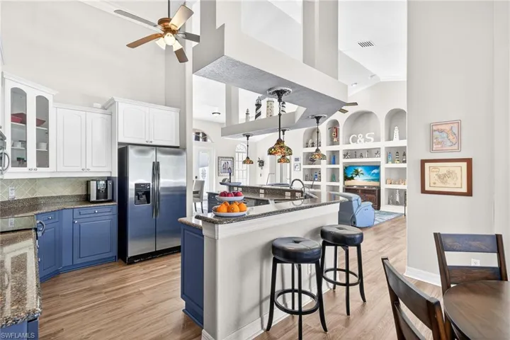 Kitchen featuring built in shelves, blue cabinetry, glass insert cabinets, a high ceiling, and dark stone countertops