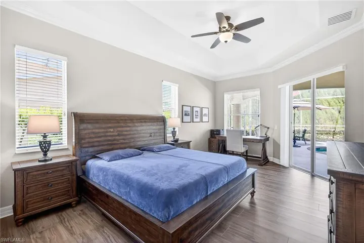 Bedroom featuring dark wood-type flooring, crown molding, ceiling fan, access to outside, and a raised ceiling