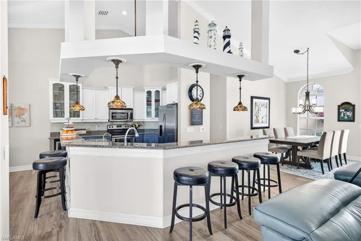 Kitchen featuring a kitchen breakfast bar, ornamental molding, glass insert cabinets, white cabinets, and hanging light fixtures