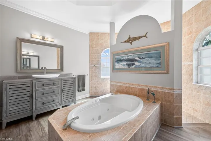 Full bath featuring a tub with jets, vanity, wood finished floors, crown molding, and tile walls