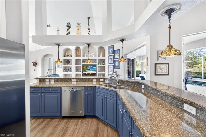 Kitchen featuring blue cabinetry, dark stone counters, appliances with stainless steel finishes, high vaulted ceiling, and hanging light fixtures