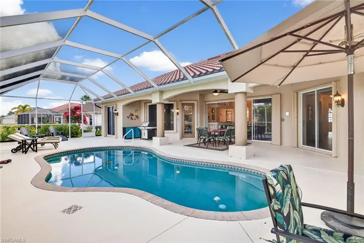 Outdoor pool with glass enclosure, a patio area, a sunroom, outdoor dining space, and grilling area