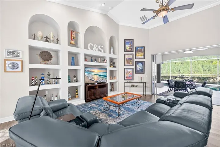 Living room featuring built in shelves, light wood-type flooring, crown molding, ceiling fan, and a sunroom