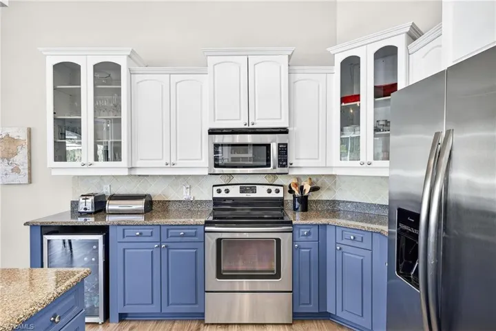 Kitchen with glass insert cabinets, blue cabinetry, appliances with stainless steel finishes, and white cabinetry