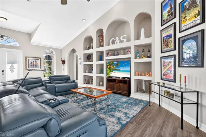 Living room featuring built in shelves, wood finished floors, a ceiling fan, vaulted ceiling, and ornamental molding