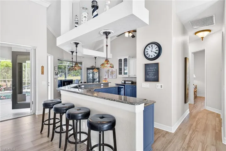 Kitchen with blue cabinets, a kitchen bar, decorative light fixtures, light wood finished floors, and an island with sink