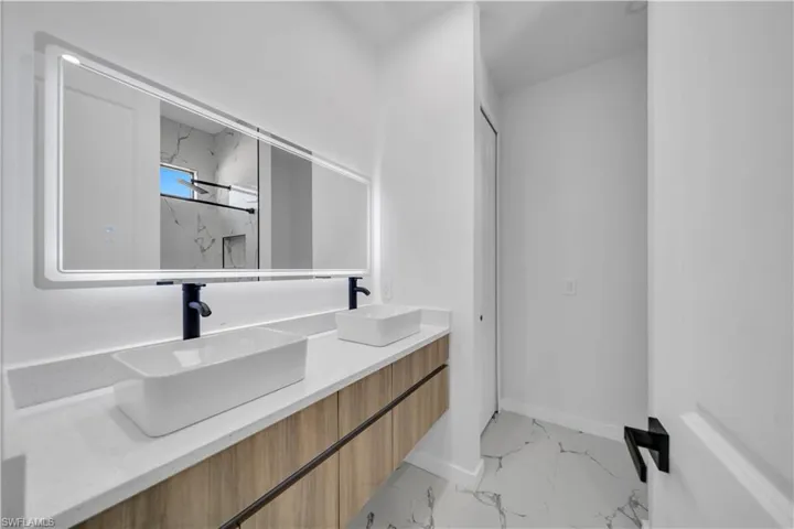Bathroom featuring double vanity, light marble finish floors, and a marble finish shower