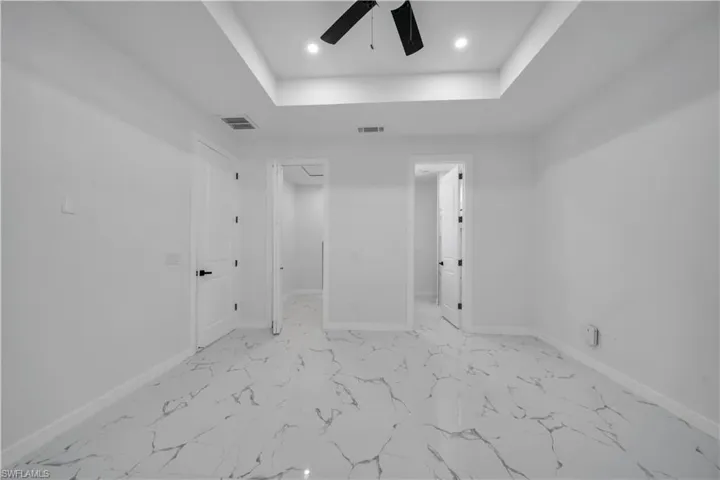 Unfurnished bedroom featuring a raised ceiling, light marble finish floors, ceiling fan, and recessed lighting