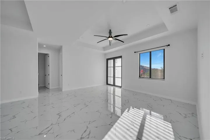 Unfurnished room with light marble finish floors, a ceiling fan, and a raised ceiling