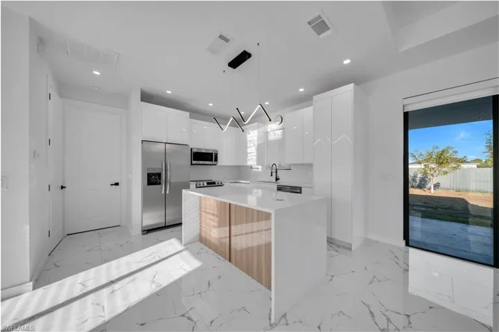 Kitchen with stainless steel appliances, a kitchen island, light stone counters, hanging light fixtures, and light marble finish flooring