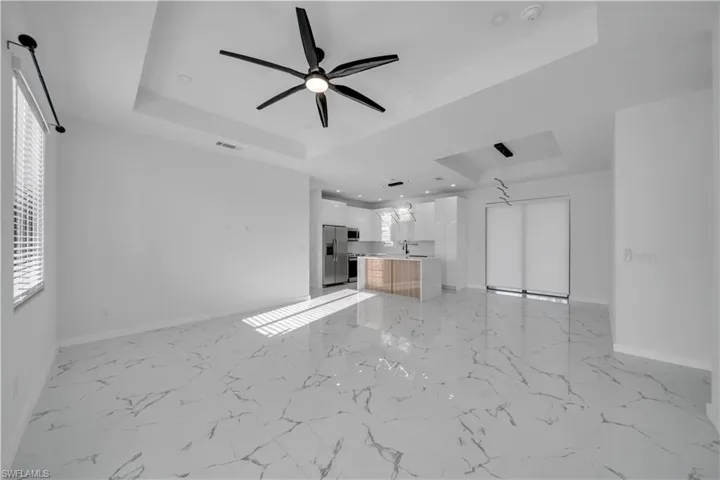 Unfurnished living room with a raised ceiling, a ceiling fan, and recessed lighting
