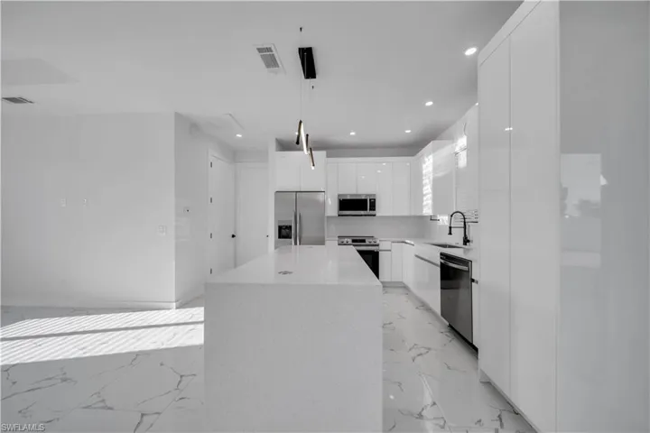Kitchen with stainless steel appliances, light marble finish floors, modern cabinets, and white cabinetry