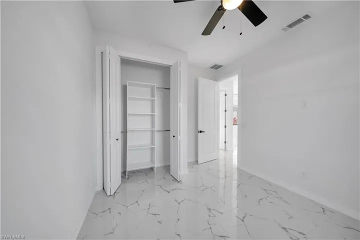 Unfurnished bedroom with light marble finish flooring, a closet, and a ceiling fan