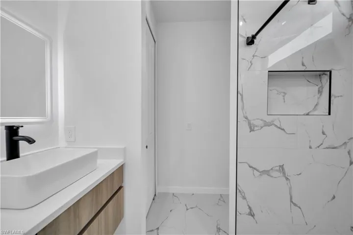 Bathroom with vanity, light marble finish flooring, and a marble finish shower