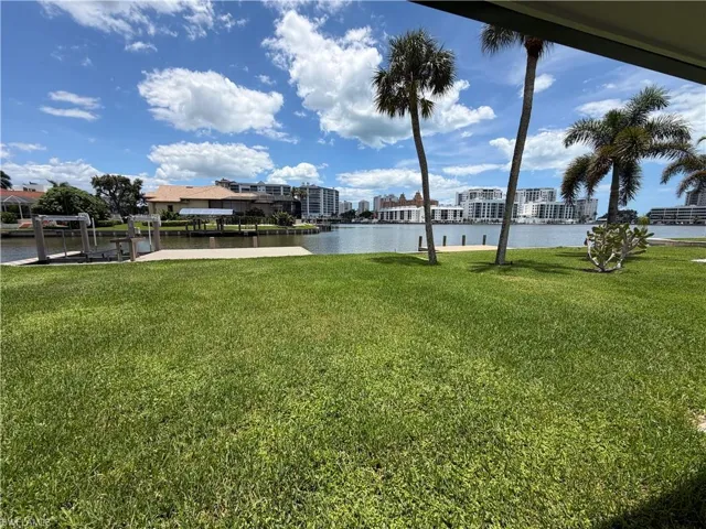 Expansive waterfront lawn featuring mature palm trees and a boat lift