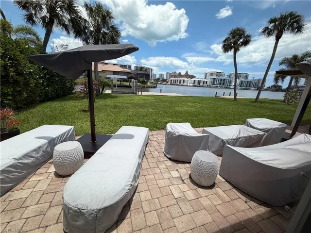 Waterfront patio with paver flooring, expansive lawn, and mature palm trees