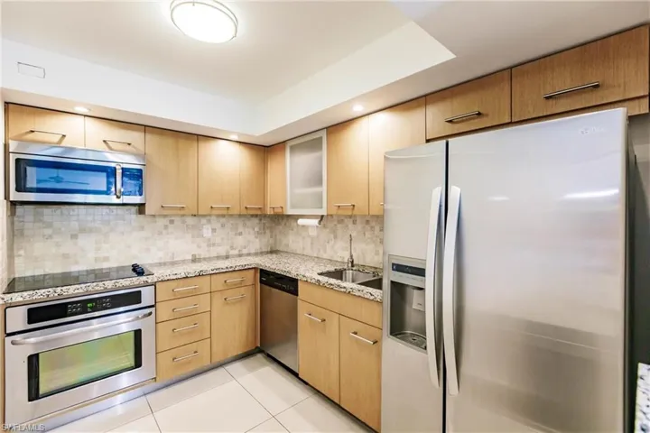 Kitchen featuring light stone counters, sink, decorative backsplash, appliances with stainless steel finishes, and light tile patterned floors