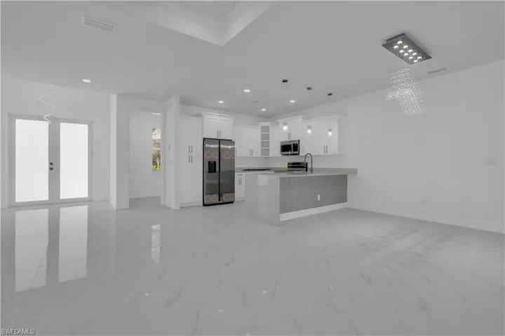 Kitchen with open floor plan, white cabinetry, stainless steel appliances, a peninsula, and suspended lighting