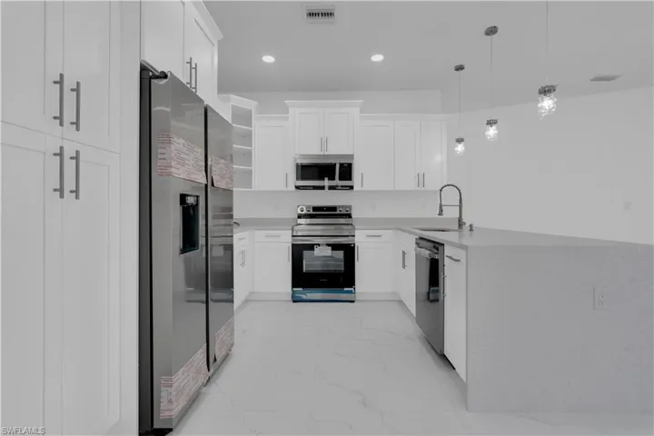 Kitchen with a peninsula, white cabinets, stainless steel appliances, light stone countertops, and decorative light fixtures