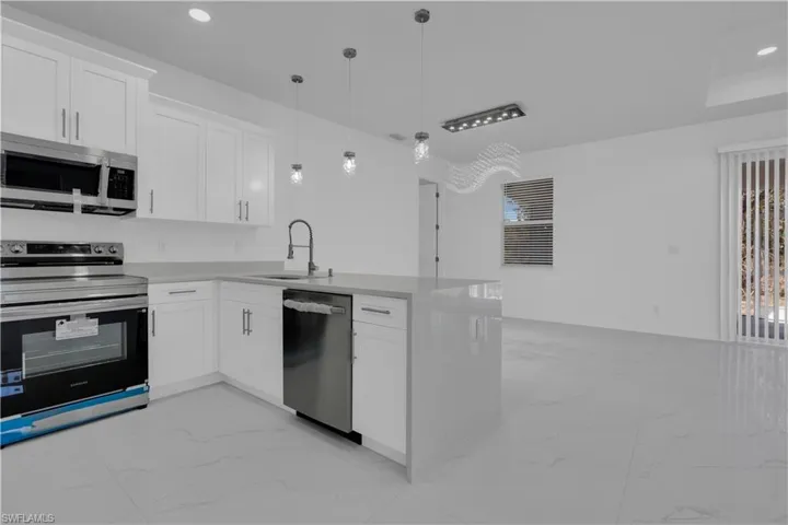 Kitchen with stainless steel appliances, white cabinetry, hanging light fixtures, light marble finish flooring, and a peninsula