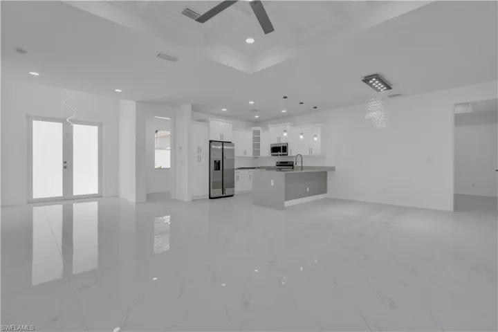 Unfurnished living room featuring coffered ceiling, ceiling fan, and a chandelier