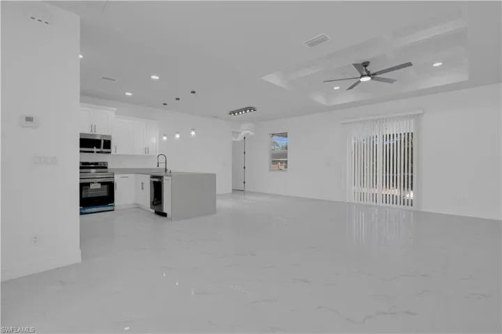 Unfurnished living room featuring coffered ceiling, recessed lighting, a ceiling fan, and light marble finish floors