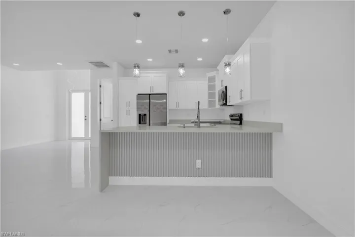 Kitchen featuring a peninsula, stainless steel appliances, white cabinetry, glass fronted cabinets, and light stone countertops
