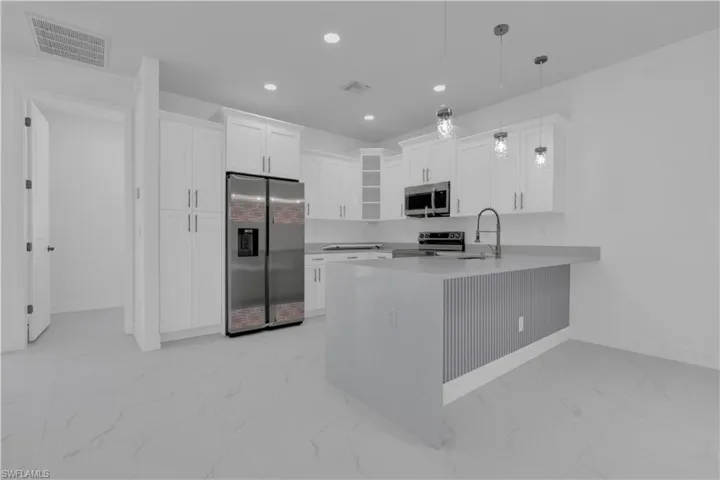Kitchen with light marble finish floors, white cabinets, stainless steel appliances, a peninsula, and hanging light fixtures