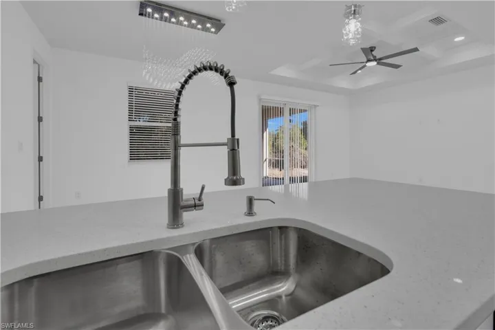 Kitchen view of coffered ceiling, light stone counters, ceiling fan, and decorative light fixtures