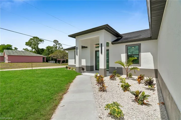 Doorway to property featuring a lawn, a shingled roof, and stucco siding