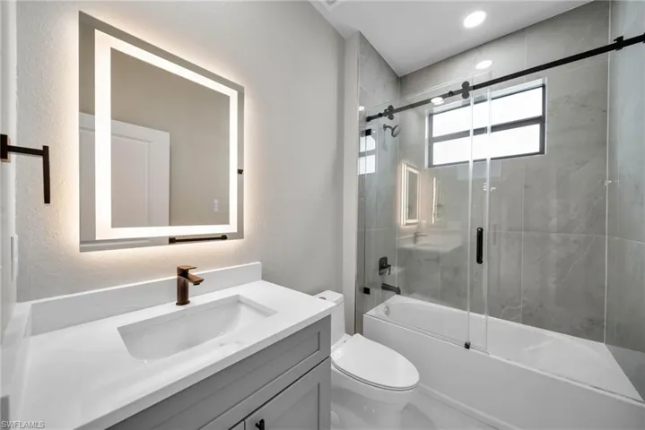 Full bathroom featuring toilet, shower / bath combination with glass door, and vanity
