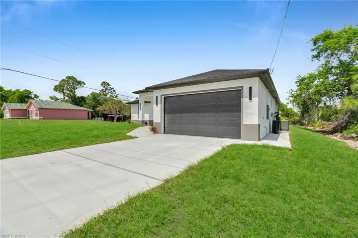 Single story home featuring driveway, central air condition unit, stucco siding, a front lawn, and a garage