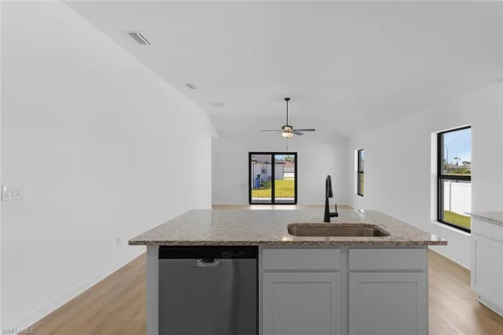 Kitchen featuring stainless steel dishwasher, light wood-style flooring, a ceiling fan, a center island with sink, and light stone counters