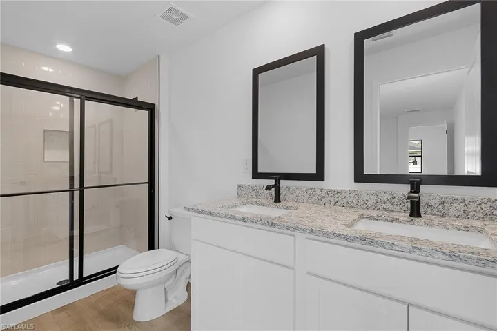 Bathroom with double vanity, a stall shower, and wood finished floors