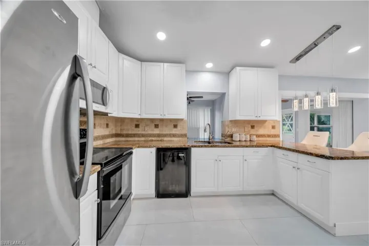 Kitchen featuring black appliances, dark stone counters, white cabinets, a peninsula, and tasteful backsplash
