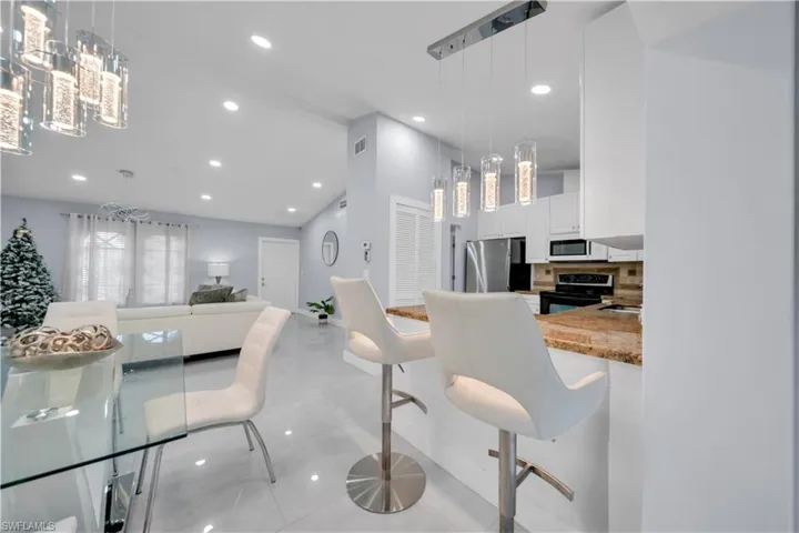Kitchen with a breakfast bar, white cabinets, range with electric cooktop, freestanding refrigerator, and light stone counters