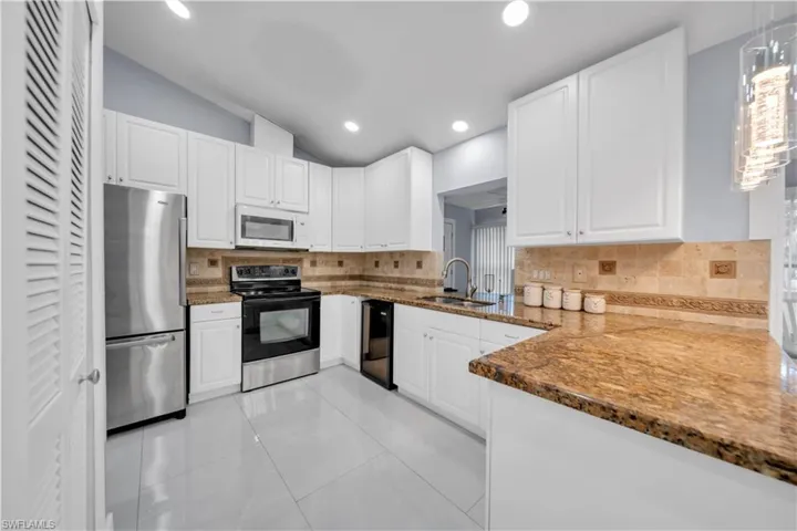 Kitchen featuring dark stone counters, white cabinets, stainless steel appliances, lofted ceiling, and light tile patterned flooring
