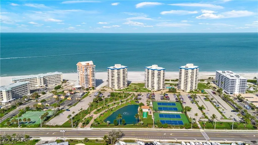 Expansive coastal property featuring multiple high-rise buildings, extensive parking areas, multiple tennis courts, and a tranquil pond