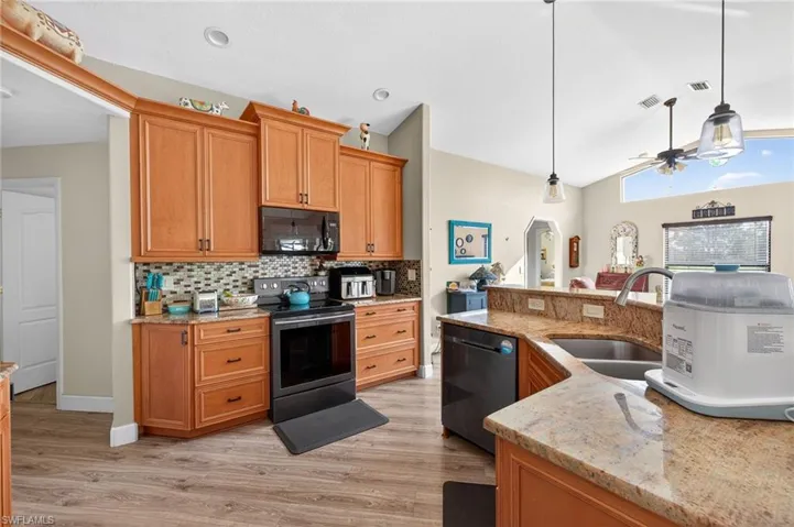 Kitchen featuring stainless steel electric stove, light stone countertops, black microwave, decorative light fixtures, and vaulted ceiling