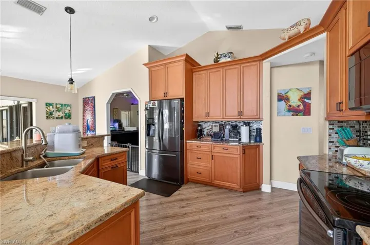 Kitchen featuring lofted ceiling, black appliances, decorative backsplash, light stone counters, and pendant lighting