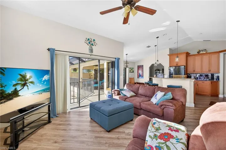 Living room with ceiling fan, light wood-style floors, and lofted ceiling
