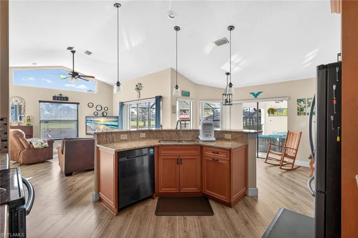 Kitchen with open floor plan, wood finish cabinets, black appliances, light wood-style flooring, and lofted ceiling